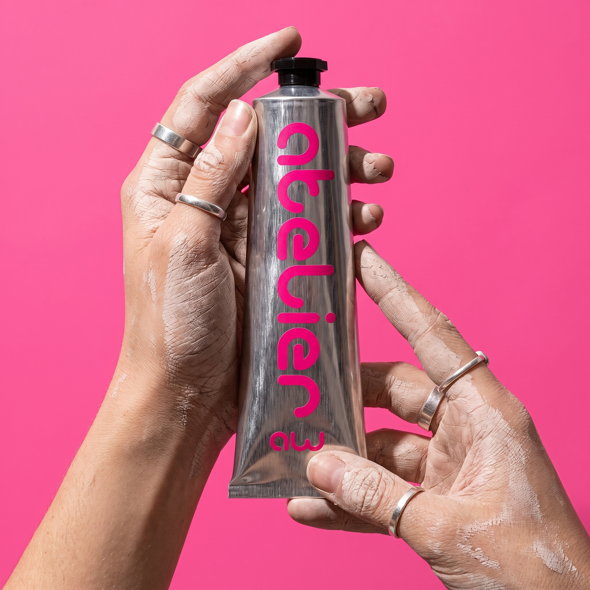 Mains de céramiste présentant le tube Gel Atelier Rose Rubis sur fond rose